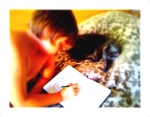 A picture of Max drawing while Furball lays beside him. The image has the tilt-shift effect.