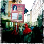 3 people in red hooded masks advertise for a Medieval Torture Museum on the streets of Old Town in Tallinn.